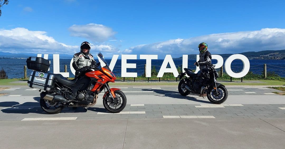 Two Open Road riders with their bikes in front of the Love Taupo sign on the Lake Taupo waterfront