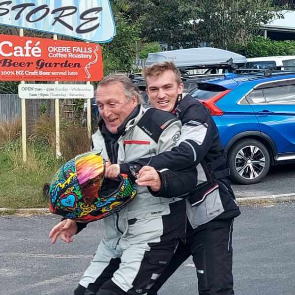 Chris and Lance in riding gear, laughing outside a cafe