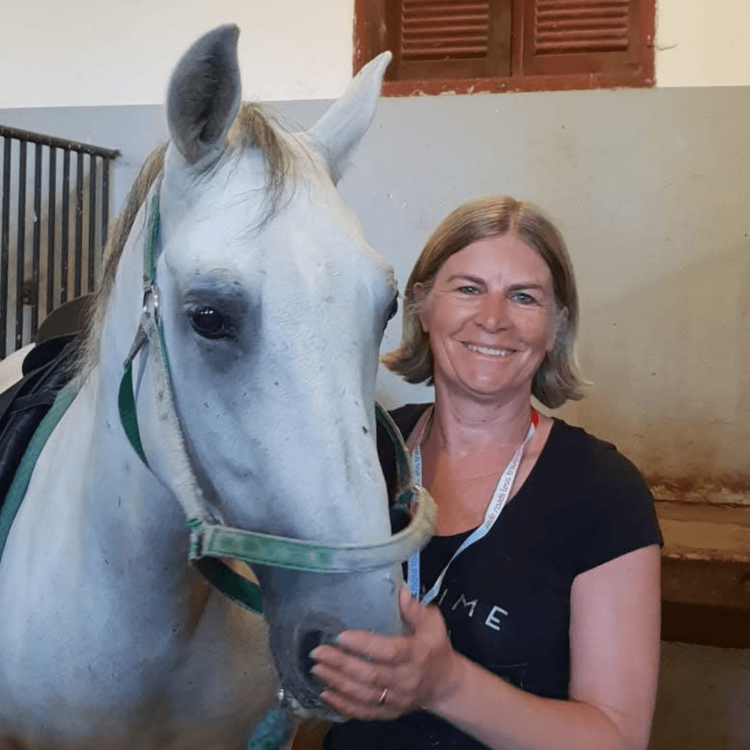 Sally smiling beside a white horse