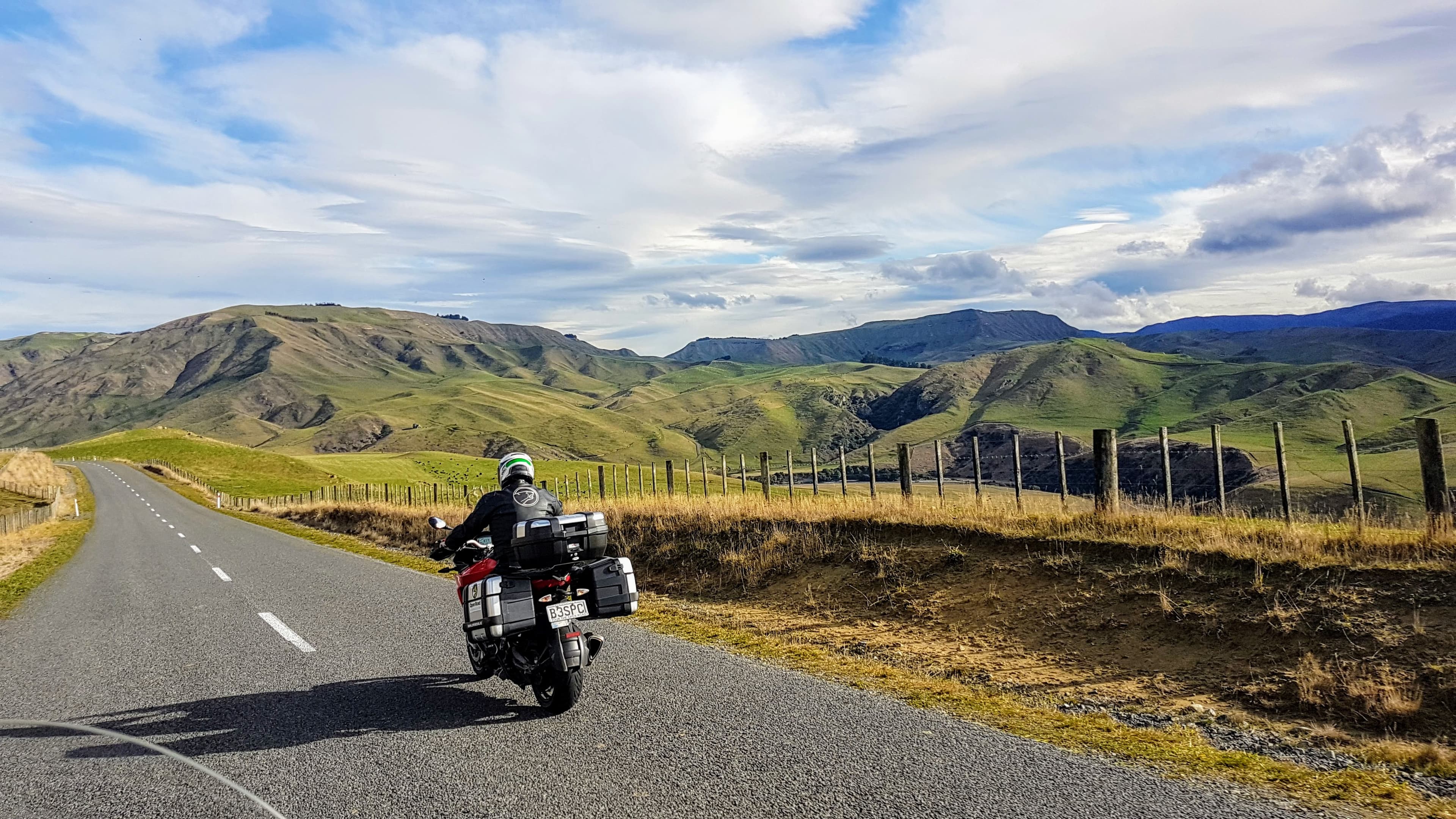 An Open Road rider on an empty country road through golden tussock hills under a wide sky